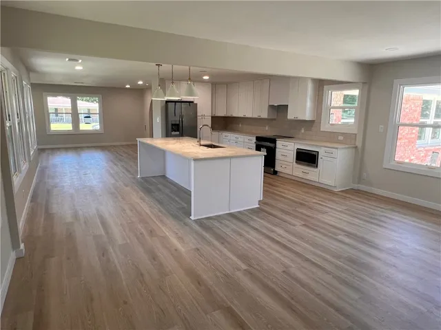 a large kitchen with stainless steel appliances granite countertop a large counter top a wooden floors and a fireplace