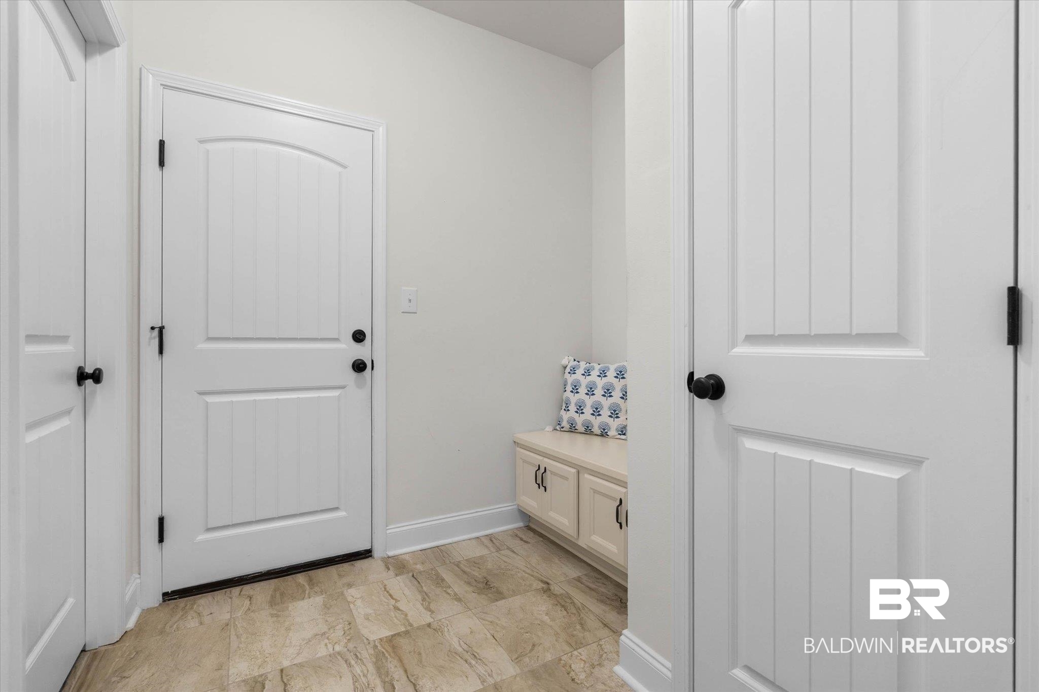1270 Surrey Loop Foley, AL 36535 - Photo 11 of 27 Entryway featuring a white paneled door with dark hardware, light-toned tile flooring, and a built-in storage bench with cabinet doors