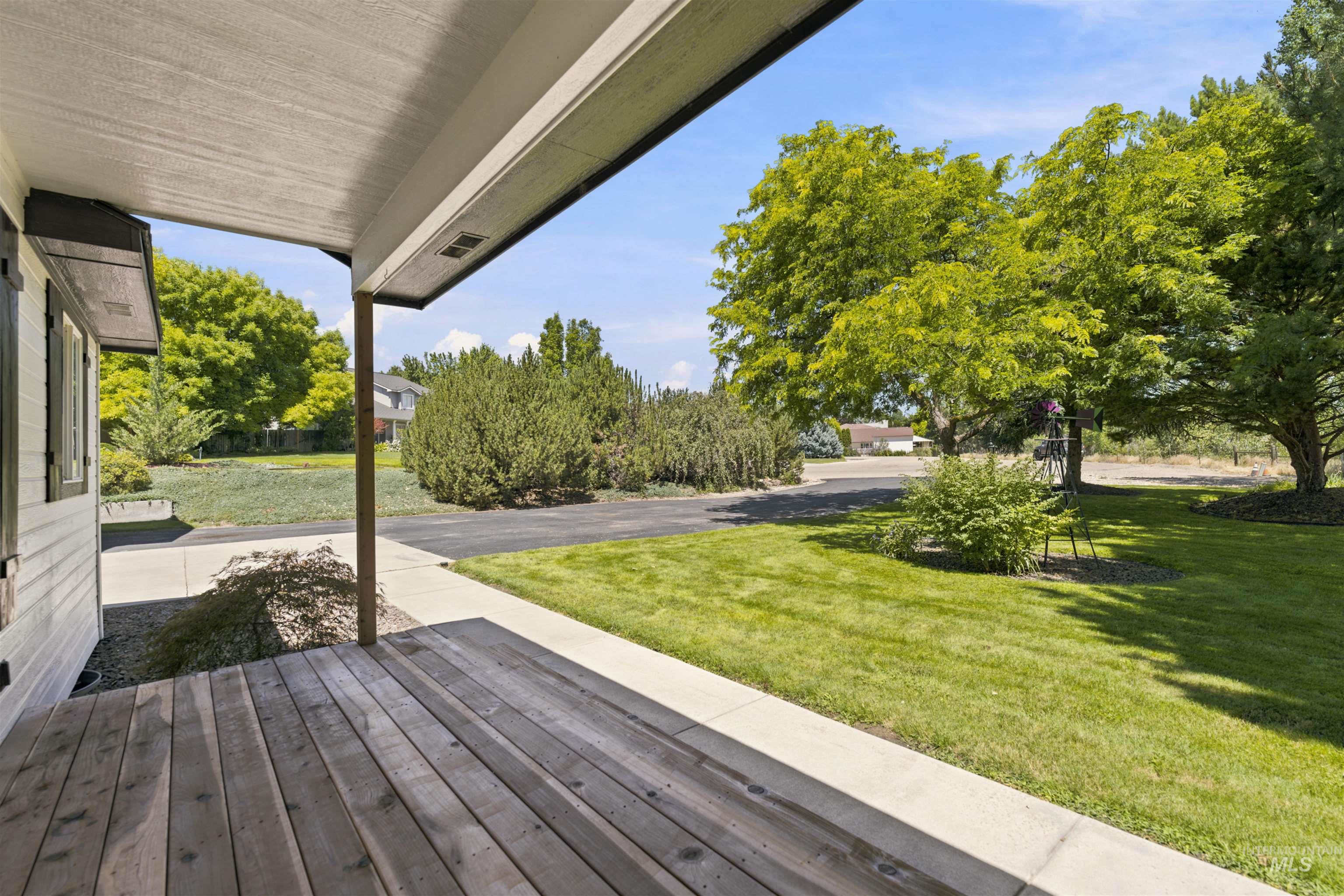 24864 Coventry Drive Caldwell, ID 83607 - Photo 31 of 49 Covered porch with wood-finish decking, supported by a structural pillar, overlooking a manicured lawn and mature trees