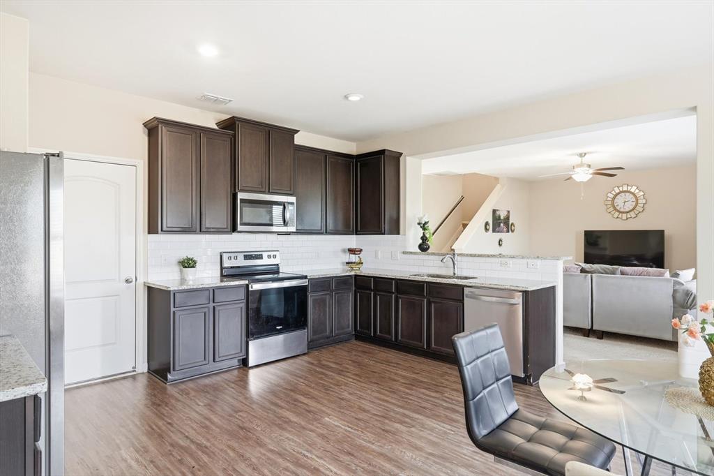 227 Curt Street Anna, TX 75409 - Photo 39 of 40 a large kitchen with stainless steel appliances kitchen island granite countertop a stove a sink dishwasher and a refrigerator with wooden floor