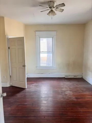 an empty room with wooden floor chandelier fan and windows