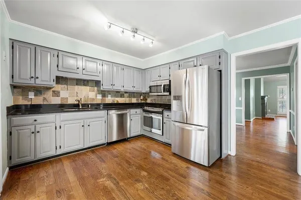 a kitchen with stainless steel appliances granite countertop a refrigerator oven a sink dishwasher and white cabinets with wooden floor