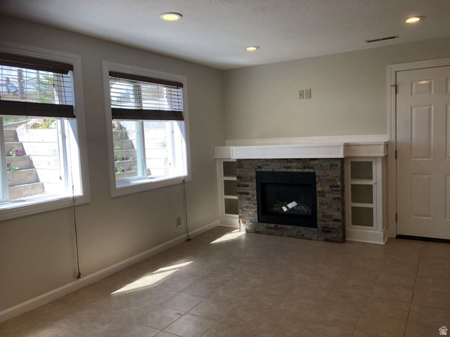 7030 West 2100 North Mendon, UT 84325 - Photo 52 of 67 Living space featuring a stone-clad fireplace with a white mantel, integrated shelving, tiled flooring, recessed lighting, and two windows with blinds