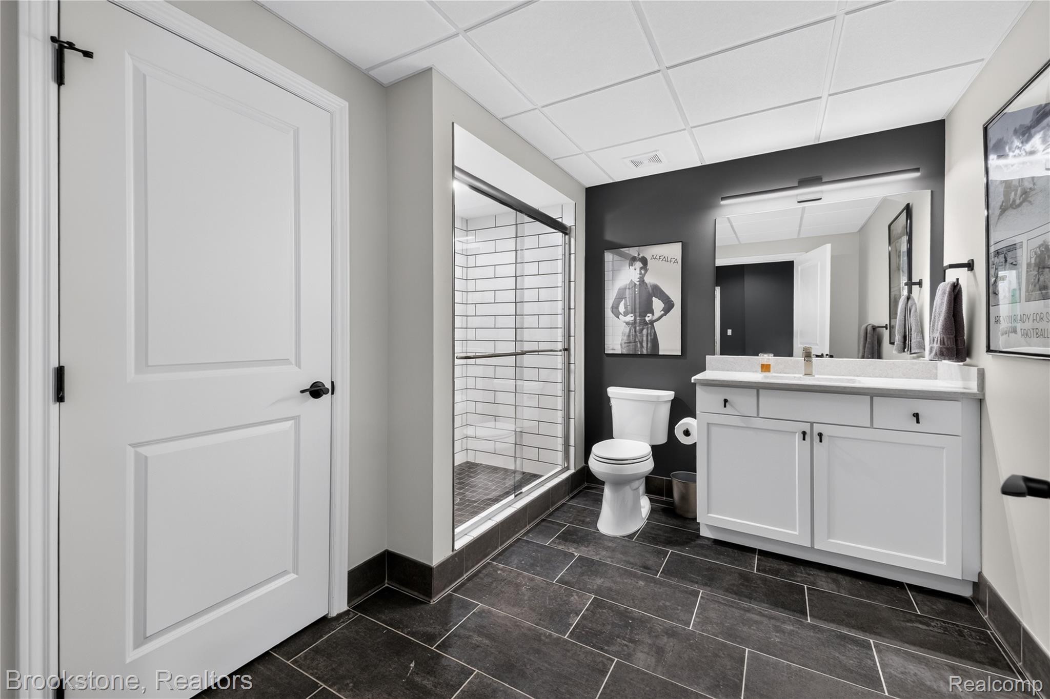 2167 Sanctuary Court Rochester, MI 48309 - Photo 28 of 68 Bathroom featuring a glass-enclosed shower with subway tile, dark large-format floor tiling, a white vanity with a light-toned countertop, and a wall-mounted mirror with integrated lighting