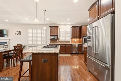 a kitchen with granite countertop a refrigerator a sink a stove and chairs with wooden floor