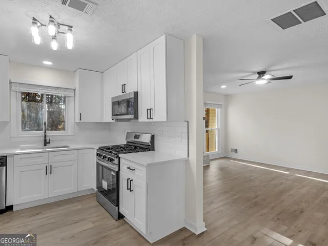 a kitchen with stainless steel appliances a sink dishwasher a stove and white cabinets with wooden floor