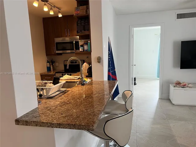 a room filed with furniture a flat screen tv and a view of kitchen