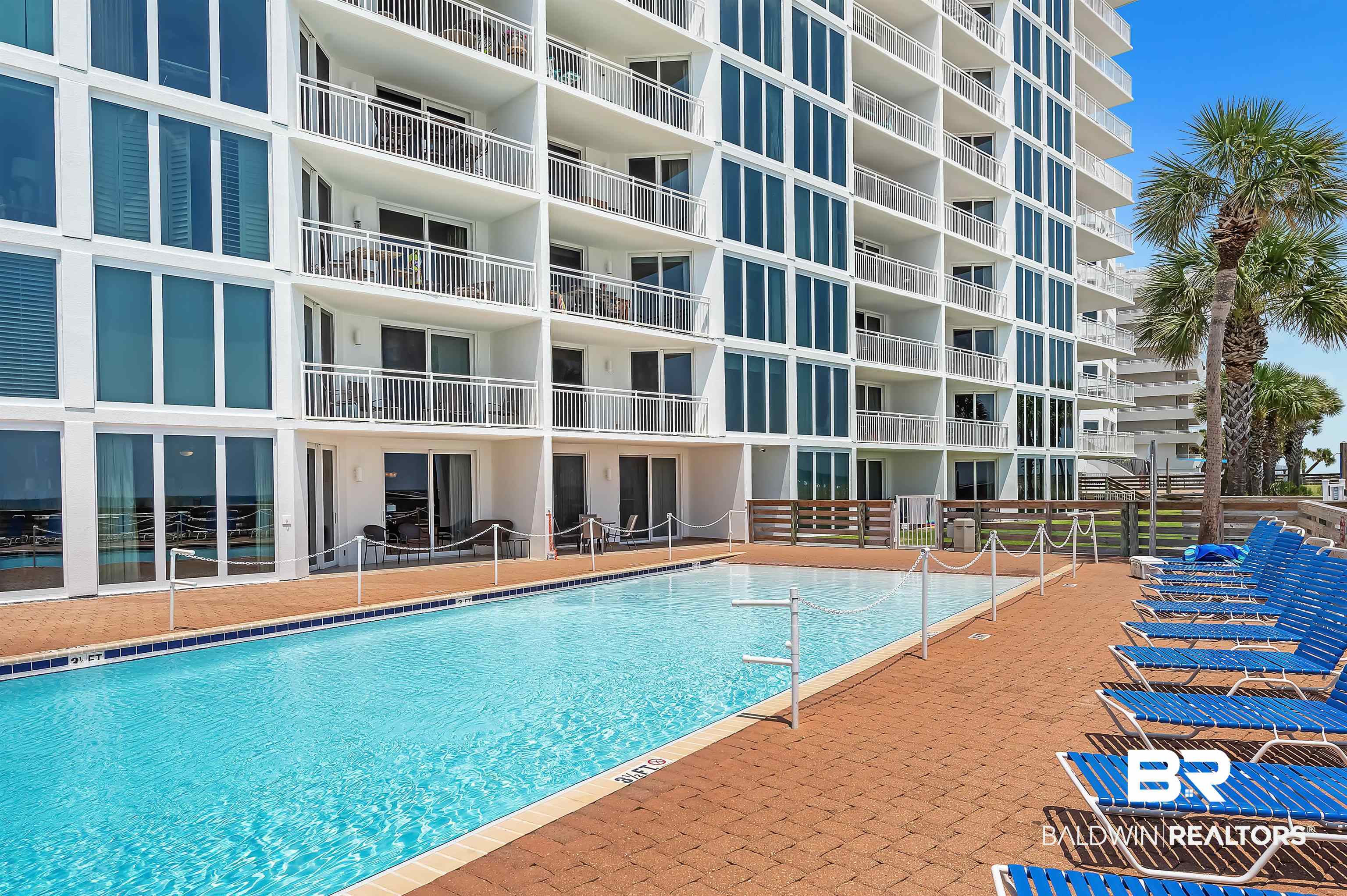 16287 Perdido Key Drive, Unit 105 Pensacola, FL 32507 - Photo 44 of 66 Outdoor swimming pool with a brick paver surround, bordered by a multi-story building featuring individual balconies and extensive window-frontage