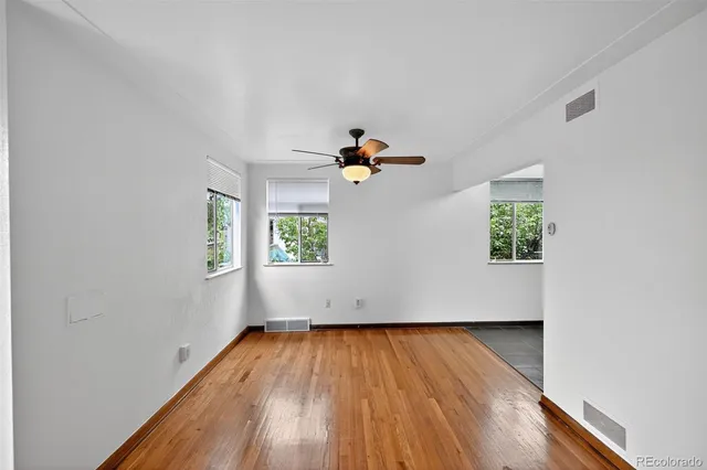 an empty room with wooden floor a ceiling fan and windows