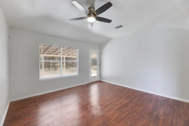 an empty room with wooden floor ceiling fan and windows