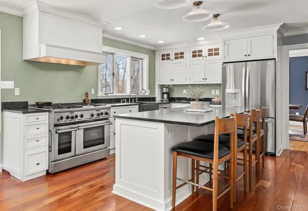 a kitchen with stainless steel appliances a stove a sink dishwasher a refrigerator and white cabinets with wooden floor