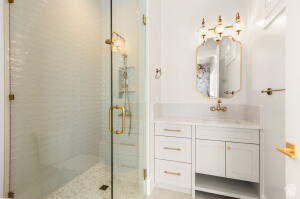 1141 East Lost Ridge Drive Washington, UT 84780 - Photo 101 of 108 Bathroom featuring a clear glass shower enclosure with brass-finish hardware, a white vanity with drawers and cabinet storage, a stone-finish countertop, and a decorative wall-mounted mirror with an ornate light fixture