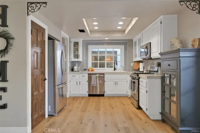 a kitchen with stainless steel appliances granite countertop white cabinets a sink a stove a microwave and wooden floors