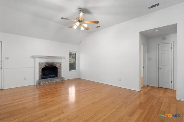 a view of an empty room with wooden floor fireplace and a window