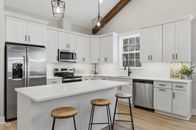 a kitchen with stainless steel appliances a stove a sink dishwasher a refrigerator with white cabinets and wooden floor