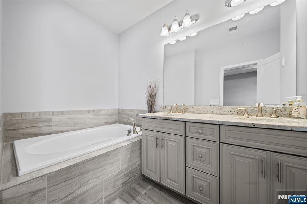 84 Truman Drive, Unit 2801 Wood-Ridge, NJ 07075 - Photo 26 of 46 a bathroom with a bathtub a double vanity sink and mirror