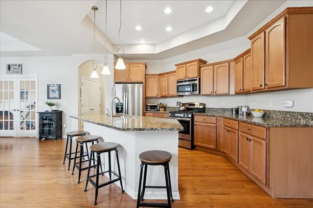 a kitchen with stainless steel appliances granite countertop a stove top oven a sink a dining table and chairs with wooden floor