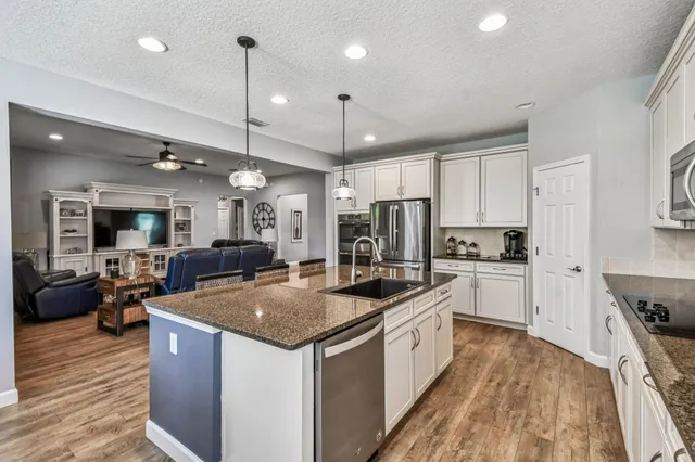 a kitchen with stainless steel appliances granite countertop a stove top oven a refrigerator a sink and chairs