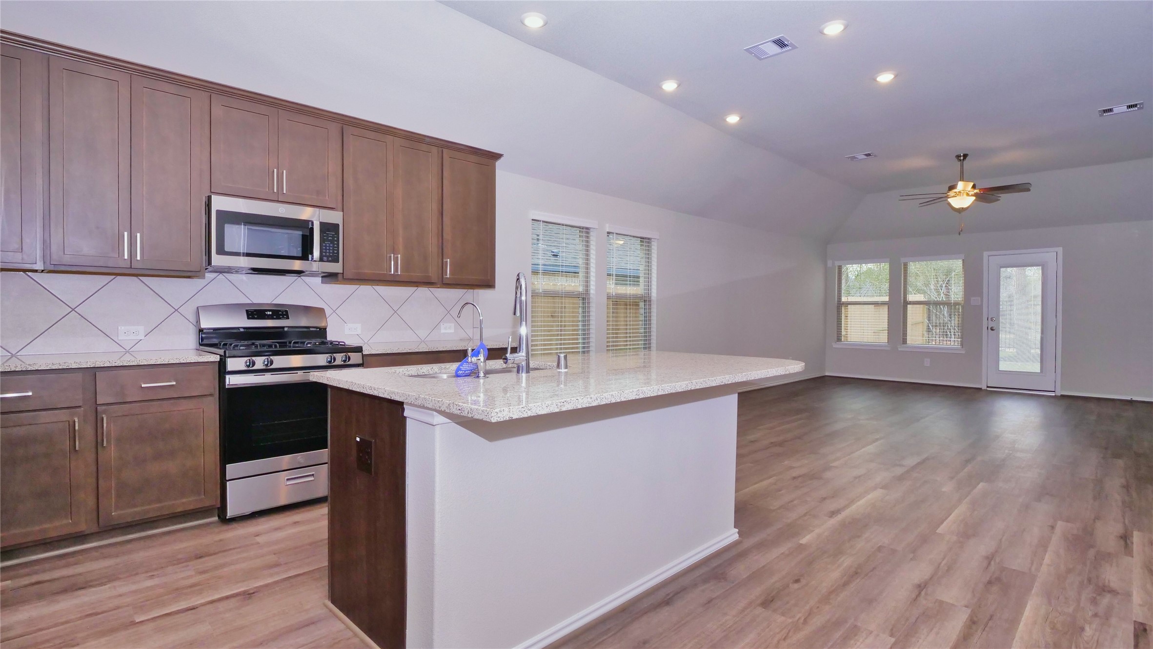 7343 Mount Greylock Loop Porter, TX 77365 - Photo 5 of 17 a kitchen with granite countertop a stove top oven a sink dishwasher and a microwave oven with wooden floor