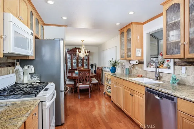 a kitchen with stainless steel appliances granite countertop a stove top oven a sink dishwasher a dining table and chairs with wooden floor