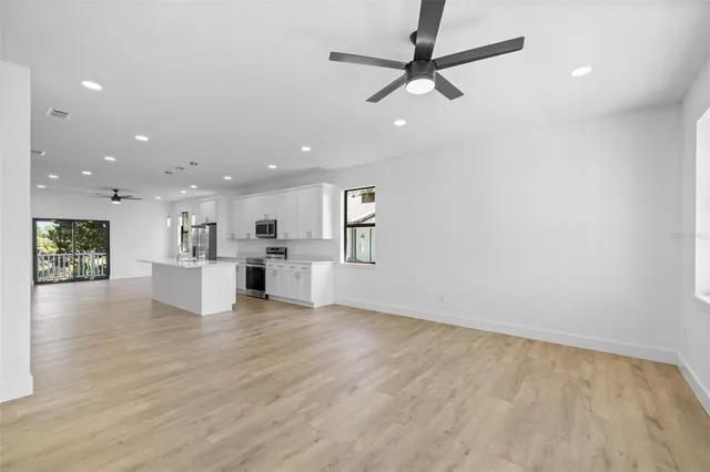 an empty room with wooden floor ceiling fan and kitchen view