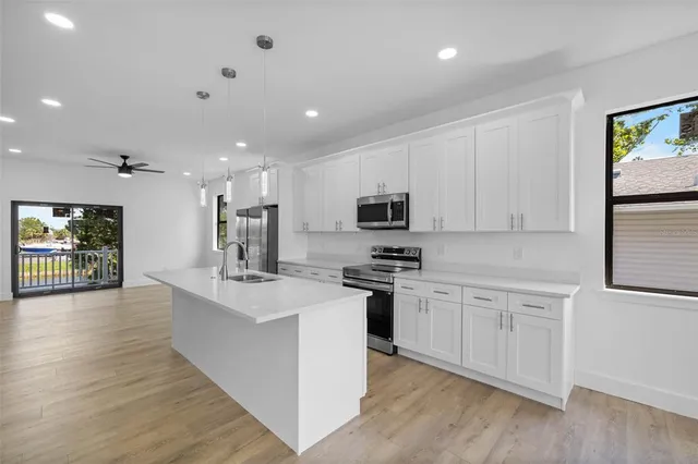 a kitchen with stainless steel appliances kitchen island granite countertop a stove a sink a refrigerator and white cabinets with wooden floor