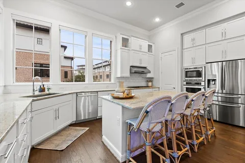 a kitchen with stainless steel appliances granite countertop a stove a sink dishwasher a refrigerator and white cabinets with wooden floor