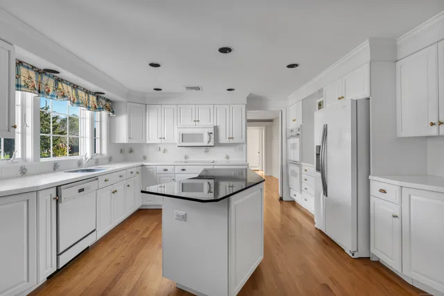 a kitchen with stainless steel appliances granite countertop a refrigerator a sink dishwasher a stove and white countertops with wooden floor