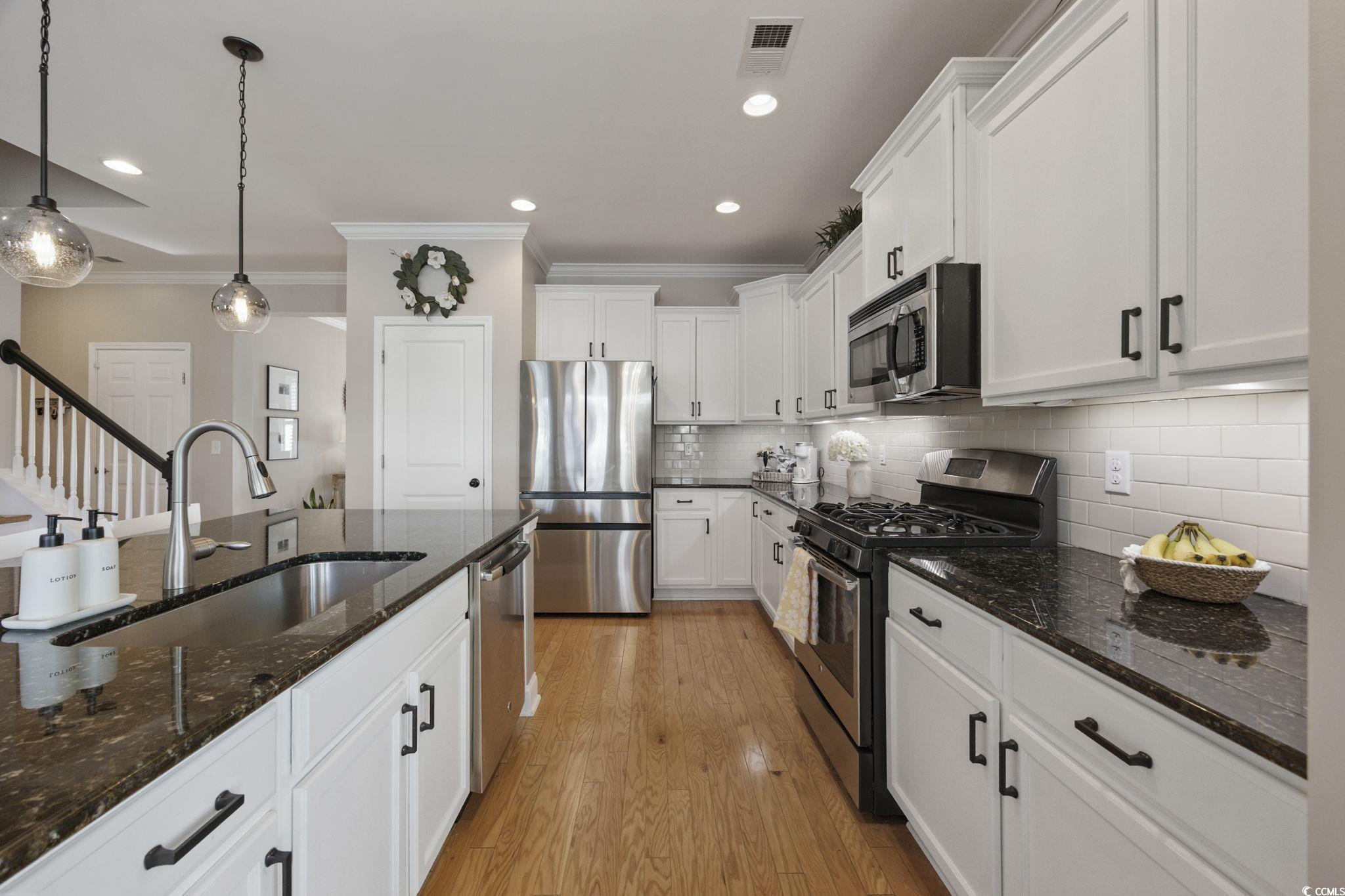 147 Hyacinth Loop Murrells Inlet, SC 29576 - Photo 4 of 40 Kitchen featuring crown molding, stainless steel appliances, dark stone counters, pendant lighting, and light wood-type flooring