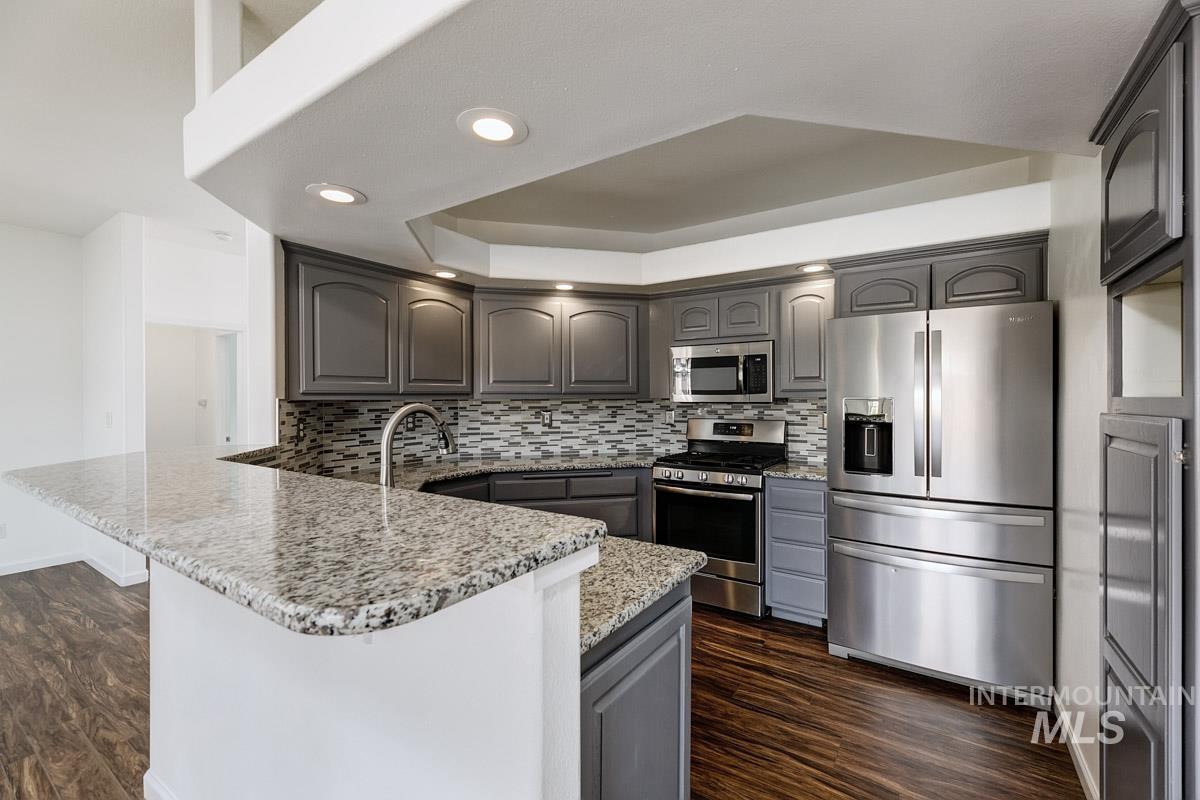 2575 S Bayou Meridian, ID 83642 - Photo 9 of 30 Kitchen featuring wood-finish flooring, stainless steel appliances, granite countertops, gray cabinetry, and a mosaic tile backsplash