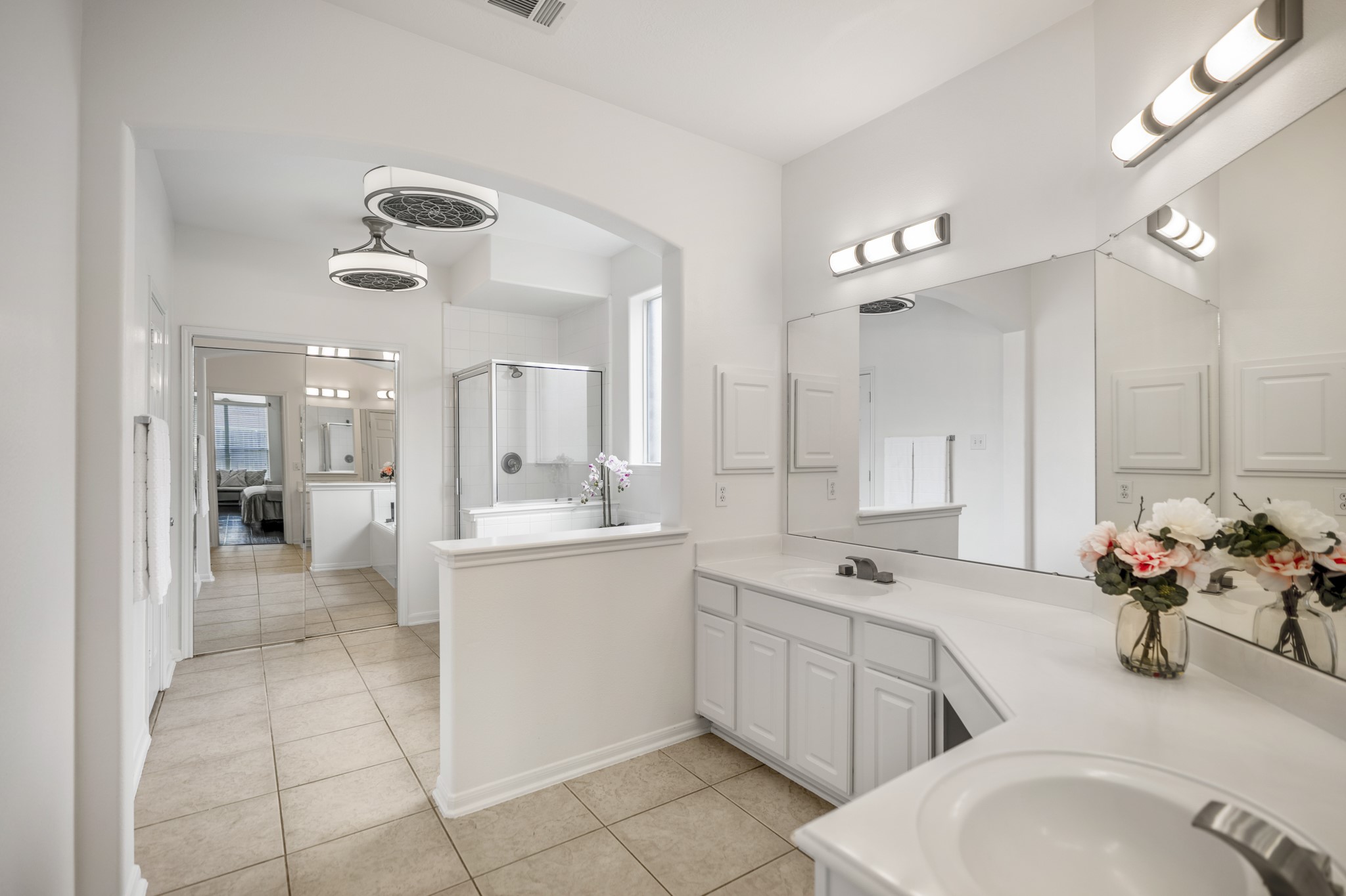 19106 South Rim Trail Spring, TX 77388 - Photo 21 of 50 Inside the primary bath, the suite continues with a bright, open layout and plenty of counter space for everyday routines. The long vanity extends along the right side, while the arched opening leads toward the soaking tub and separate shower area. Mirrored doors at the back reflect the bedroom beyond, helping show how the bath, closet area, and primary suite connect in one easy flow.