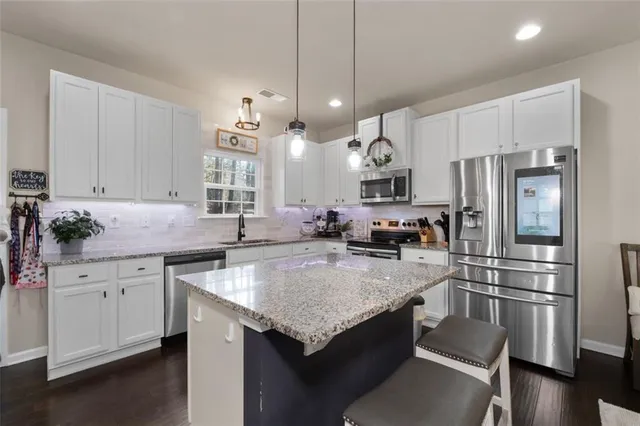 a kitchen with granite countertop stainless steel appliances a sink dishwasher a refrigerator a stove and white cabinets with wooden floor