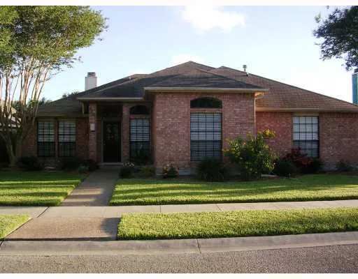 a view of a brick house with a yard plants and large trees