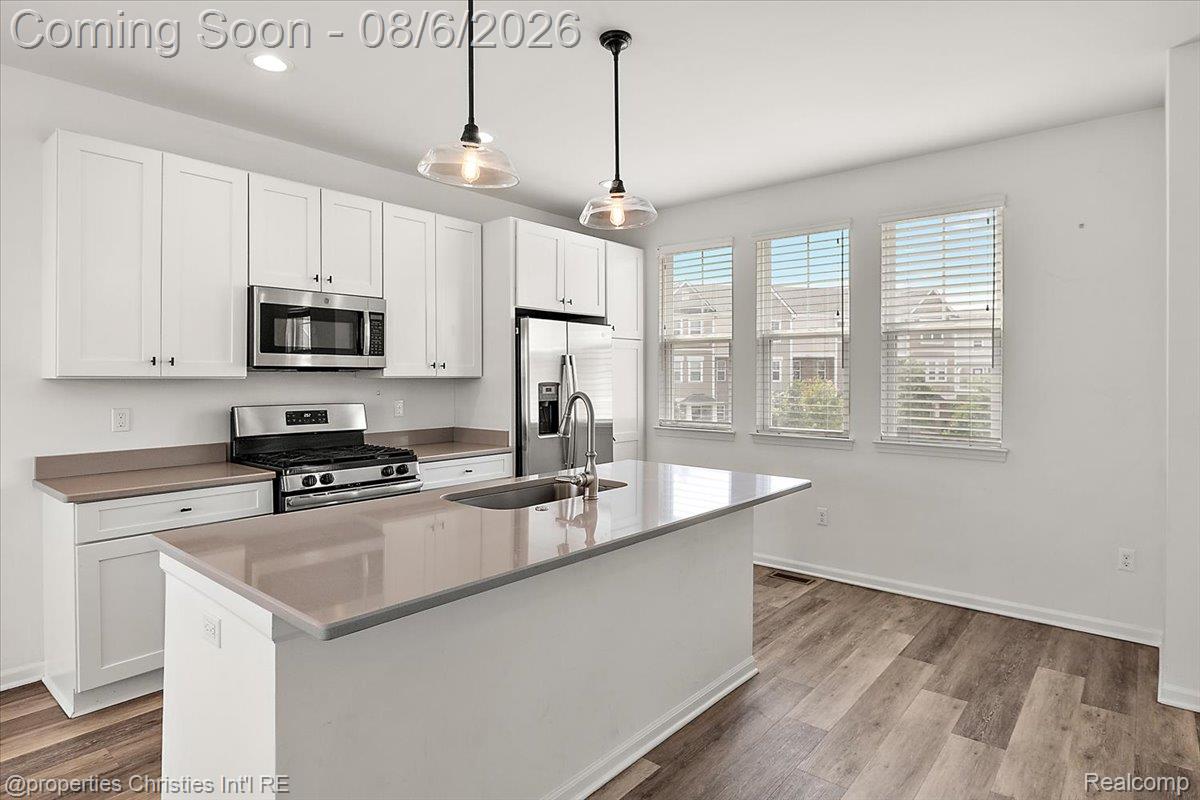 Contemporary kitchen featuring white cabinetry, stainless steel appliances, a center island with sink, and wood-finish flooring