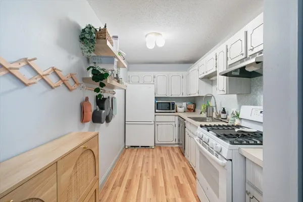 a kitchen with granite countertop a refrigerator a stove a sink dishwasher and white cabinets with wooden floor