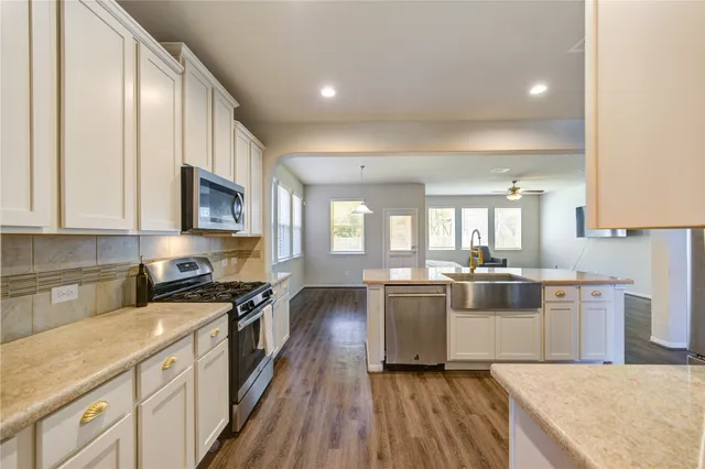 a kitchen with stainless steel appliances granite countertop a stove top oven a sink dishwasher and white cabinets with wooden floor