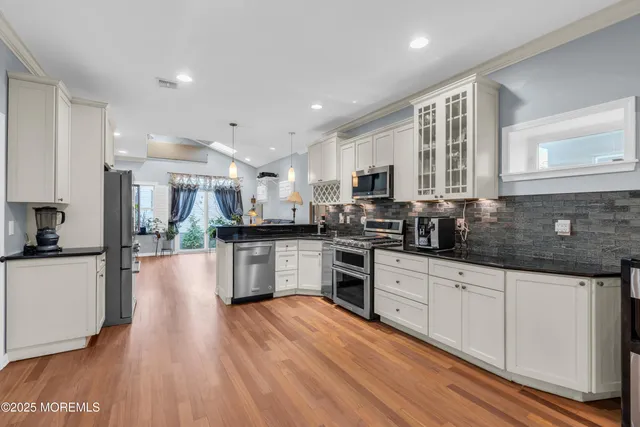 a kitchen with stainless steel appliances granite countertop a stove top oven a sink a refrigerator white cabinets and wooden floor