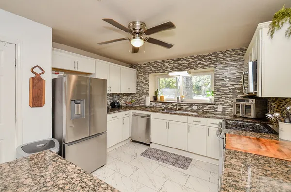 a kitchen with stainless steel appliances granite countertop a refrigerator a sink and white cabinets