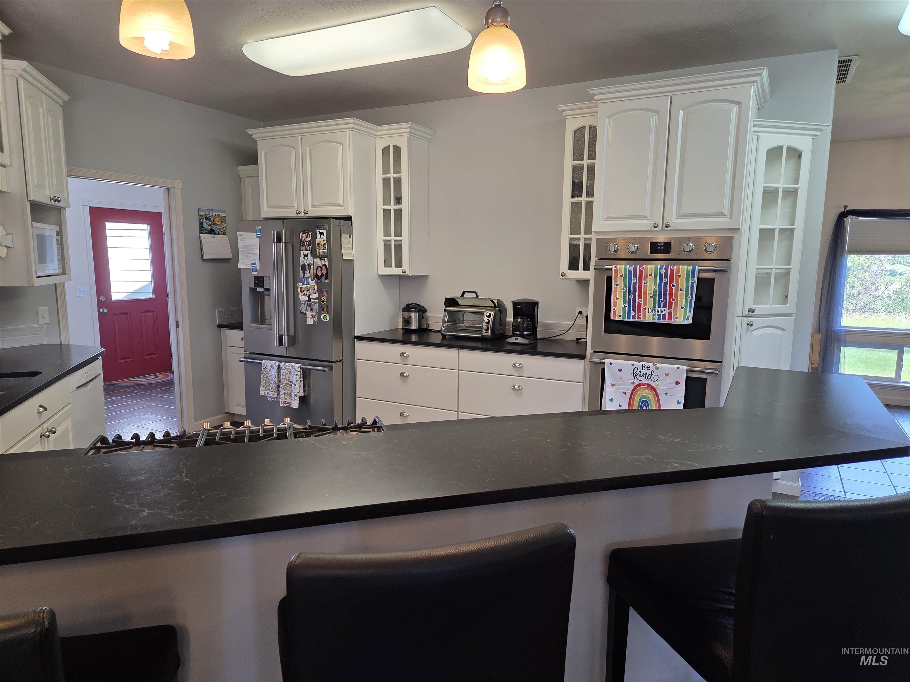 1085 Wallen Road Moscow, ID 83843 - Photo 11 of 50 Modern kitchen featuring white cabinetry with glass-front accents, dark countertops, and stainless steel appliances including a built-in oven and refrigerator