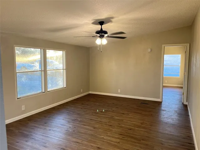 an empty room with wooden floor chandelier fan and windows