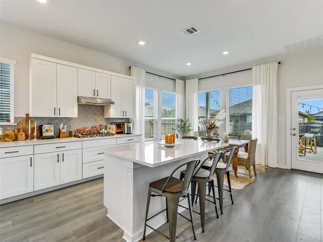 a kitchen with stainless steel appliances granite countertop a stove a sink a refrigerator white cabinets with wooden floor dining table and chairs