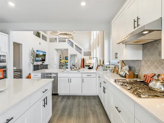 a large white kitchen with a stove a sink dishwasher and white cabinets with wooden floor