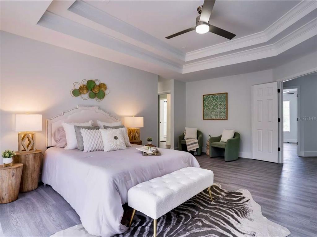 7724 US Open Loop Lakewood Ranch, FL 34202 - Photo 17 of 40 a spacious bedroom with a bed a couch and a chandelier