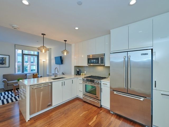 a kitchen with stainless steel appliances a stove a sink dishwasher a refrigerator and white cabinets with wooden floor
