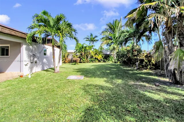 a backyard of a house with table and chairs plants and large tree