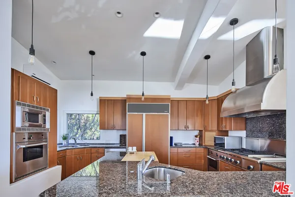 a kitchen with granite countertop a stove a sink a refrigerator and a wooden cabinets