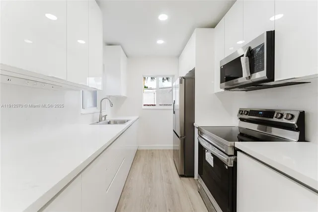 a kitchen with stainless steel appliances a sink dishwasher a stove top oven a refrigerator with grey cabinets and wooden floor