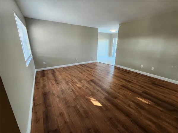 a view of an empty room with wooden floor and a window