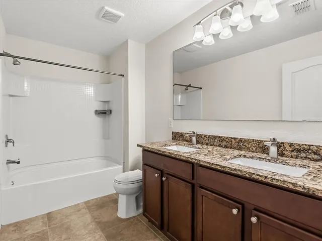a bathroom with a granite countertop sink a toilet a mirror a bathtub and shower