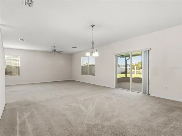 an empty room with chandelier fan and windows